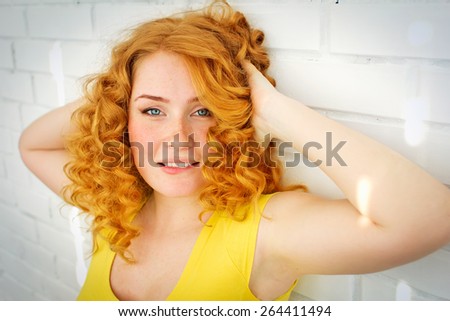 the red-haired blue-eyed girl with freckles in spots of sunlight on a white brick wall