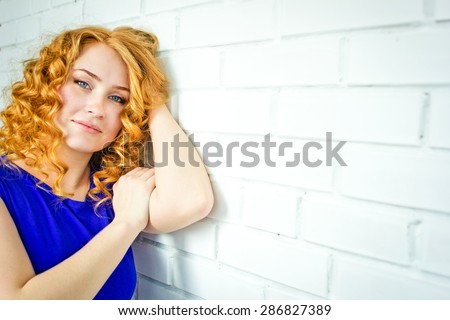 the red-haired blue-eyed girl with freckles and curly hair against a white brick wall