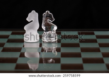 Two glass knight chess pieces on a glass board.