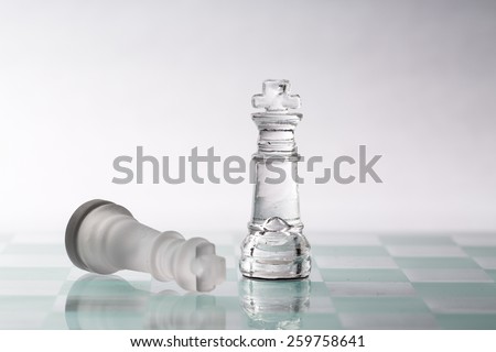 Two kings from a glass chess set on a glass board.   One piece is standing and one is laying down.