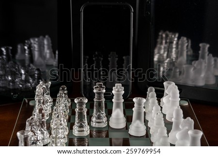 Entire glass chess set on glass chess board with two tablets and smart phone positioned to show reflections.
