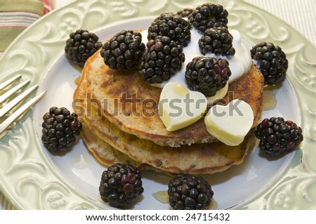 Healthy whole grain pancakes topped with yogurt, blackberries, and heart shaped butter.