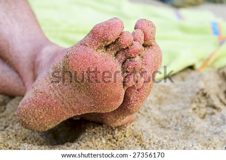 Sandy feet rest on the beach with a beach towel in the background.