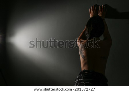 Model from behind, standing against a dark wall, showing her tattoo against envy people