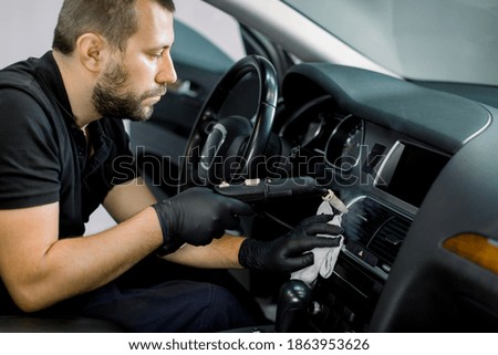 Disinfecting the car interior, steam heat disinfection of vehicles. Close up of young bearded man worker, cleaning car air conditioner and control panel with high pressure hot steam cleaner