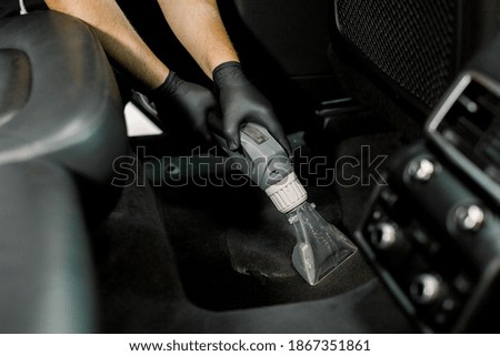 Details of car vacuum cleaning. Professional male worker using wet vacuum cleaner for dirty car interior. Auto car service worker using vacuum cleaner to wash car floor with foam