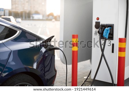 Power supply connect to modern blue electric car for recharging the battery. Automobile at charge station