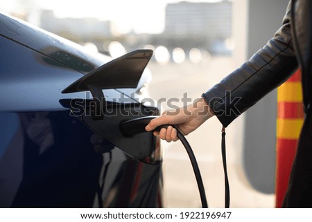 Cropped view of female hand, holding power cable supply plugged in electric car, charging automobile battery from city EV charging station