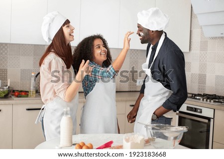 Baking is fine and funny. Happy curly mixed race teen girl smutching her father\'s face with flour, while having fun with her parents in the kitchen, baking together
