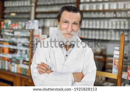 medicine, pharmacy, people, health care and pharmacology concept - smiling senior male pharmacist in white coat standing indoors with arms crossed in beautiful ancient pharmacy interior