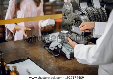 Unrecognizable woman customer making payment in ancient drugstore, bying the medicine. Pharmacist man holding terminal, and swiping patient's credit card credit card