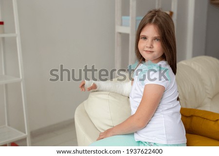 Child with a cast on a broken wrist or arm smiling and having fun on a couch. Positive attitude, recovery and kid concept.