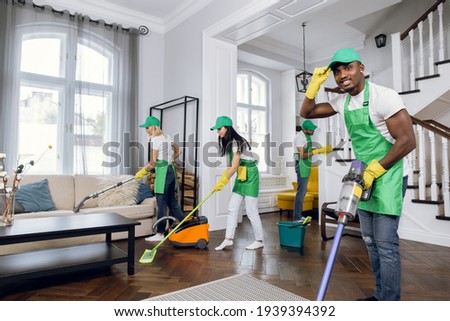Professional mixed race janitors in uniform doing spring cleaning of modern house. Team of cleaners using various special tools during working process. Modern customer service.