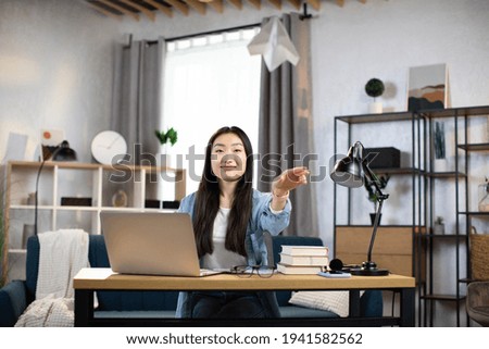 Smiling female freelancer playing with paper plane while working from home. Attractive asian woman taking break during working time.