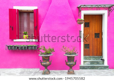Door and windows with flowers on the pink facade of the house. Colorful architecture in Burano island, Venice, Italy.