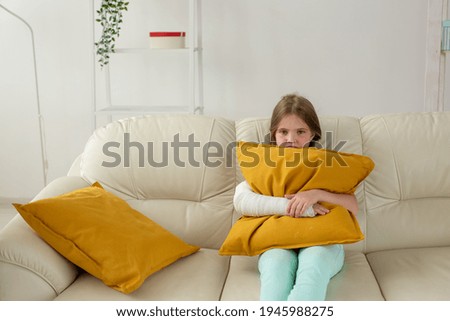 Child with a cast on a broken wrist or arm sitting on a couch. Recovery and disease concept.