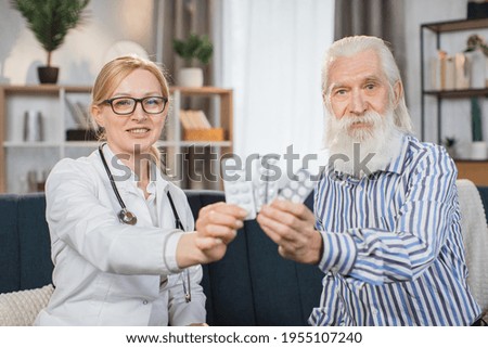 Healthcare, medical care at home. Close up portrait of likable 40-aged blond woman doctor, sitting on sofa with her pleasant 60-aged bearded man patient and demonstrating to camera blisters with pills