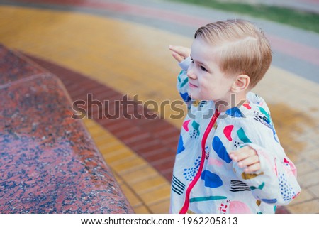 A young cute happy 4 years old boy posing and playing outside, wearing colorfull jacket