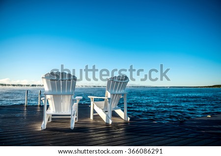 Muskoka chairs on a dock at a blue lake with a blue sunrise and mist coming off the water, closeup