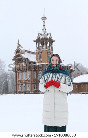 Russian tourist woman in Pavlovo Posad shawl, scarf. Wooden house, Astashovo terem with ornamental carved windows, frames in Chukhloma, Kostroma region, Russia. Russian style in architecture. Landmark