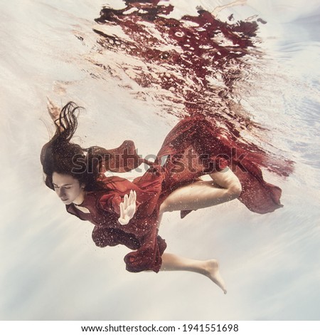 A girl in a fluttering red dress swims underwater as if flying in zero gravity