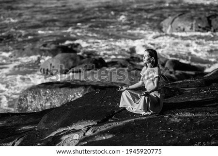 Yoga woman sit on the rocks on ocean beach. Black and white photo.