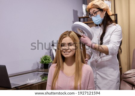 Trichological and dermatological examination of the scalp and hair follicles of young caucasian female patient in a cosmetology clinic, client is smiling enjoying while visiting dermatologist