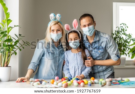 Dad, mom and child daughter at the table in medical masks are painting Easter eggs for the holiday. Happy easter family quarantined coronavirus. Happy at home.