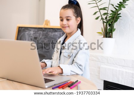 Smart little Caucasian girl child sit at table study at laptop make notes write in notebook, small schoolgirl handwrite prepare homework assignment at home, distant education concept