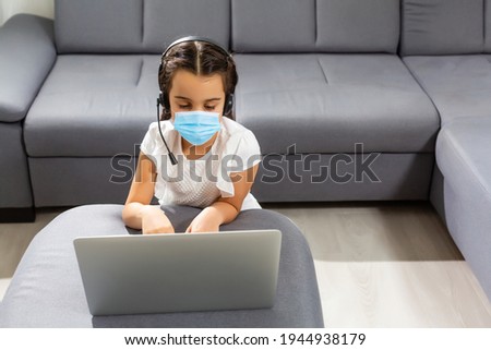 Little kid schoolgirl 12-13 years old in face mask study at desk with pc laptop isolated on pastel pink background. School distance education at home during quarantine concept. Holding hands folded