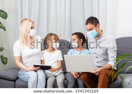 Family waving and greeting someone during video call at home. Parents are wearing protective face masks.
