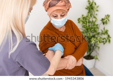 cheerful young nurse giving a vaccine injection to elderly woman at home