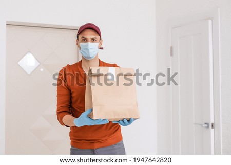 Young delivery man in medical gloves and protective face mask holding paper bags in hands. Man courier with shopping bag. Safe online delivery from supermarket to home. COVID-19 coronavirus protection