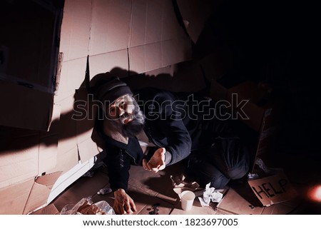 A homeless bearded man sits on boxes on street and asks for help. Need a homeless person asks for money for food and overnight.