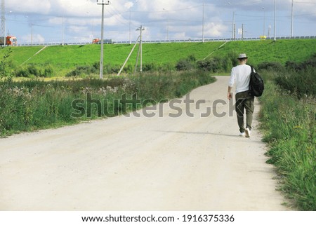 A man walks along a country road. Hitchhiker around the country. A man stops a passing car on road.