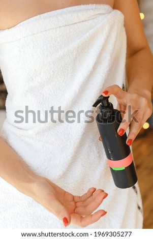 Beautiful fresh young woman applying cream or body wash on hand from dispenser indoors