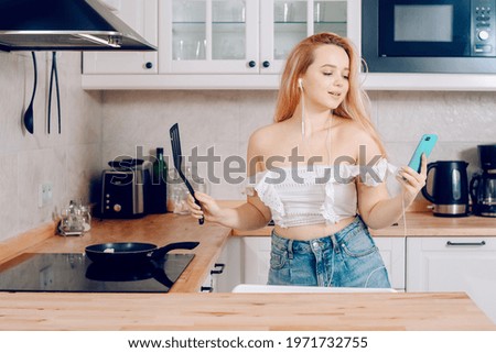 Woman singing and dancing in the kitchen with a smartphone, music.A girl in headphones with a phone stands in the kitchen and prepares food behind an induction stove