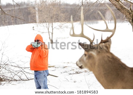 Deer hunter in orange taking aim at a whitetail deer. Focus on hunter.