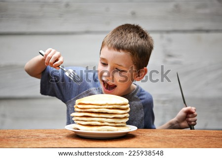 Young boy eating a stack of pancakes.