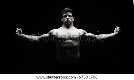 Low key artistic fitness man on black. Highlights muscular build of model.