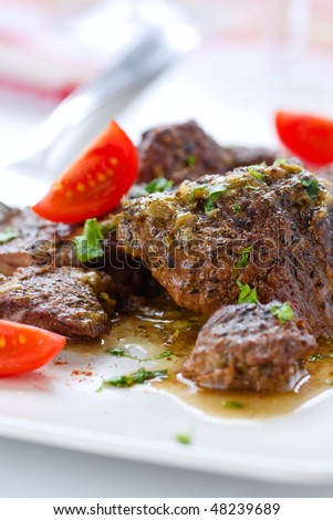 Stewed beef with cherry tomatoes and herbs on the white plate,closeup