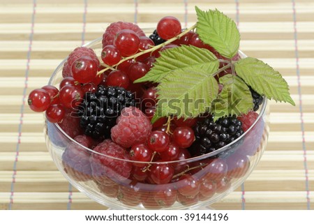 Different sorts of berries with leaves in a glass