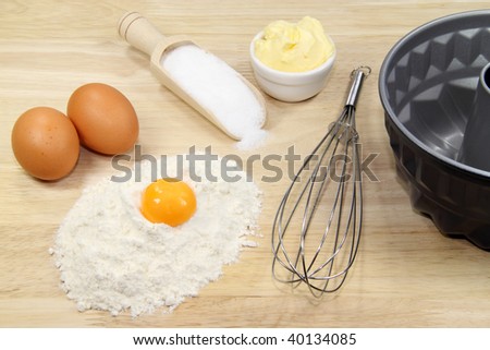 Baking ingredients with eggbeater and cake pan on a wooden kitchen board