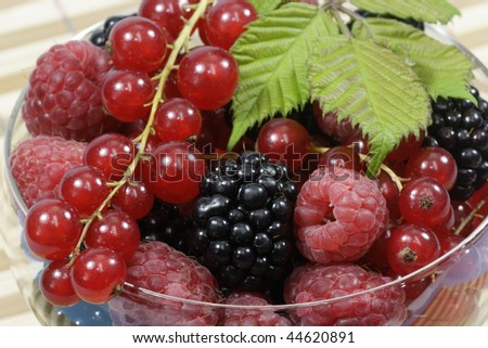 Different sorts of berries with leaves in a glass