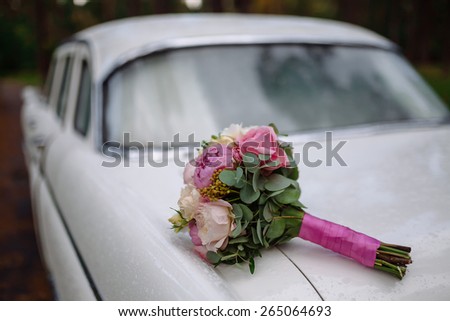 wedding bouquet of flowers and greenery lying on the trunk of a white retro car