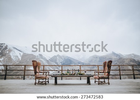 garnished and served with a table and two chairs for two vintage on a wooden terrace with views of the mountains and the snow-capped peaks