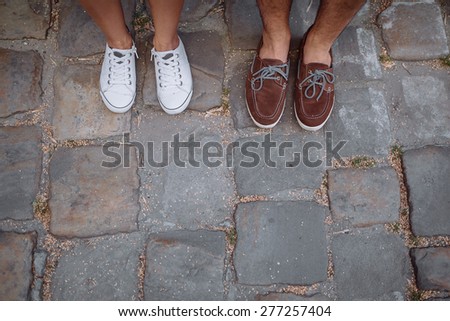 guy in a brown Top-Siders and girl in white sneakers standing on the pavement of paving
