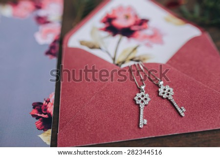 jewelry in the form of keys on a chain lying on the envelope color marsala with greeting card on a background of vintage wooden planks