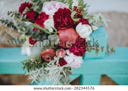 bridal bouquet of pomegranate fruit, peony, pinks and greens lying on a fence turquoise