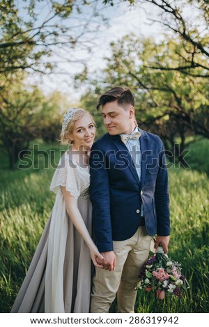 couple in wedding attire with a bouquet of flowers and greenery is in the hands against the backdrop of the garden at sunset, the bride and groom